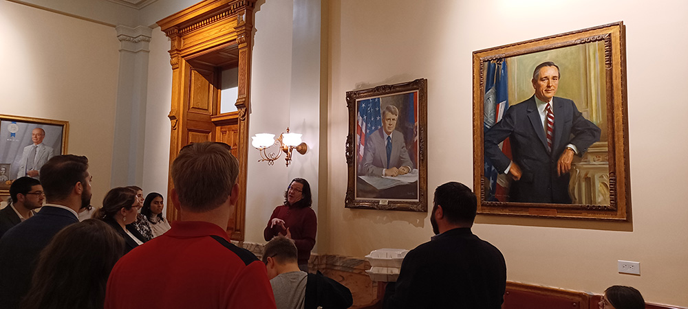 A staff member standing in front of portraits talks about the art collection to a small group of visitors