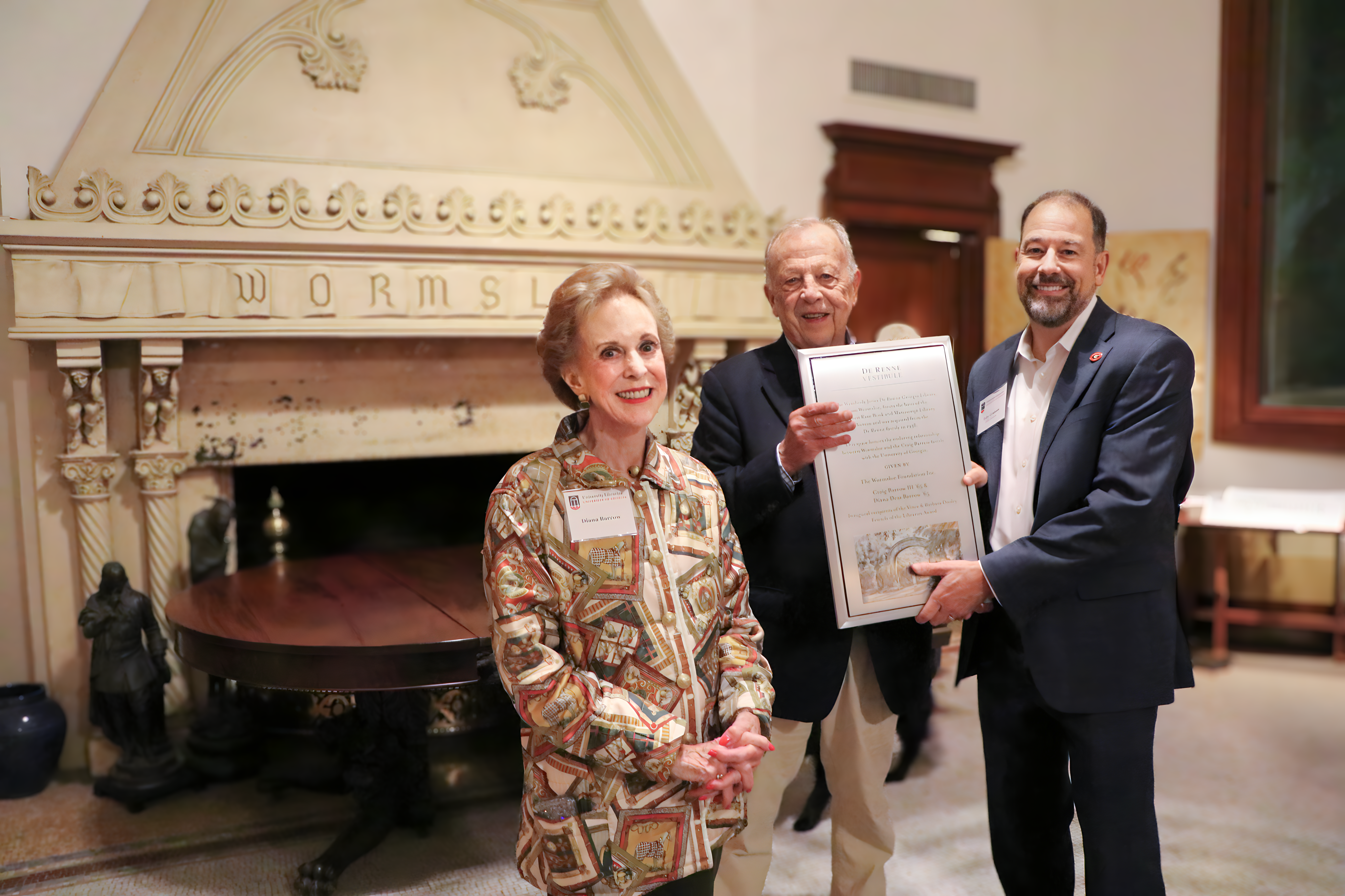 Diana Barrow with Craig Barrow, holding a plaque with Toby Graham in the historic Wormsloe library