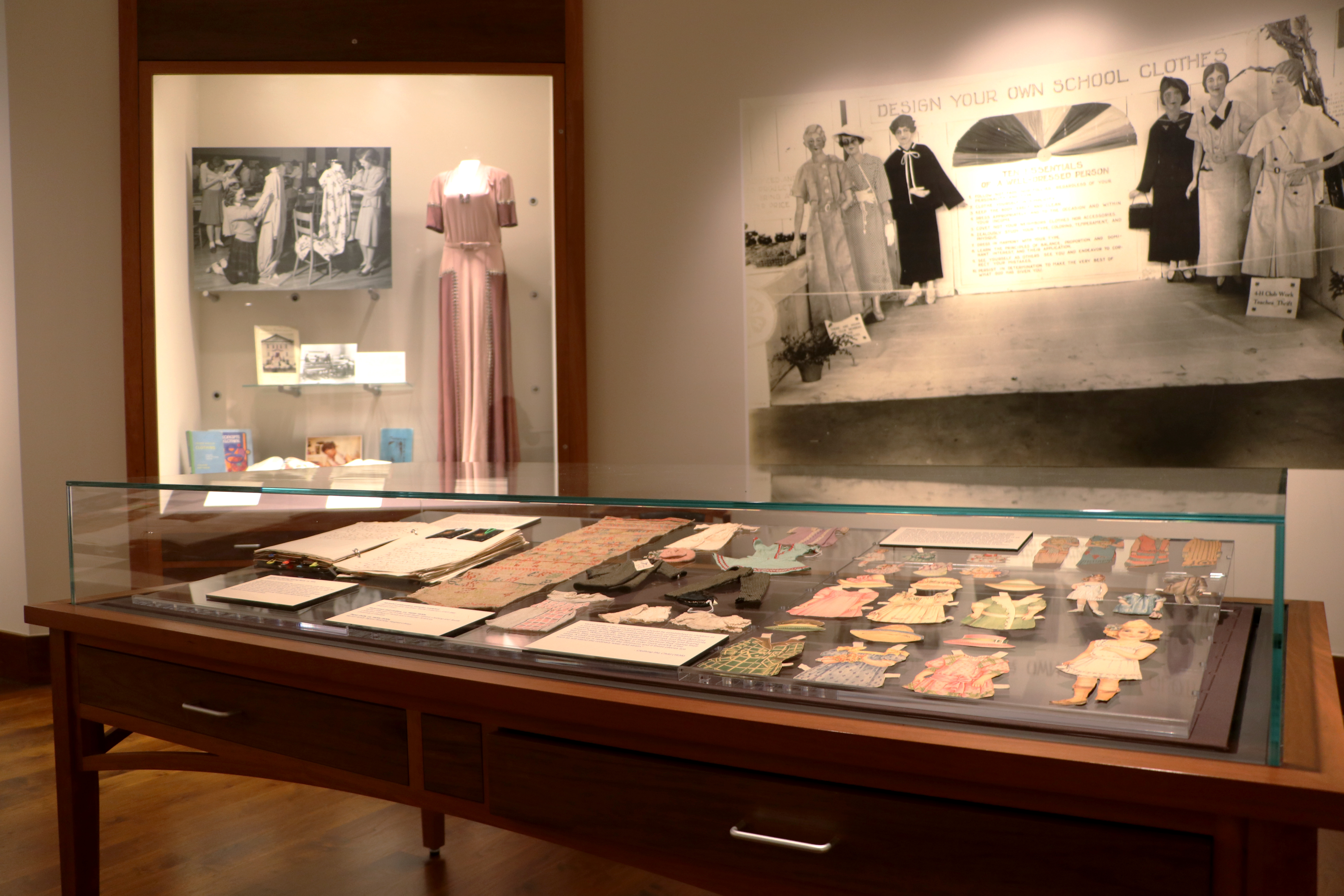 display case with paper dolls, dresses, and photos