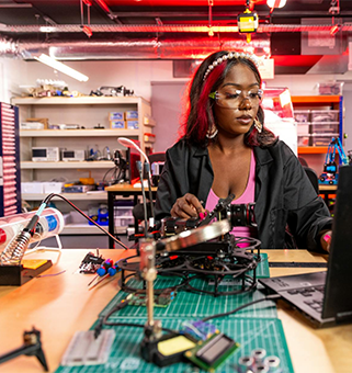 student seated in front of soldering project with laptop in a workspace setting