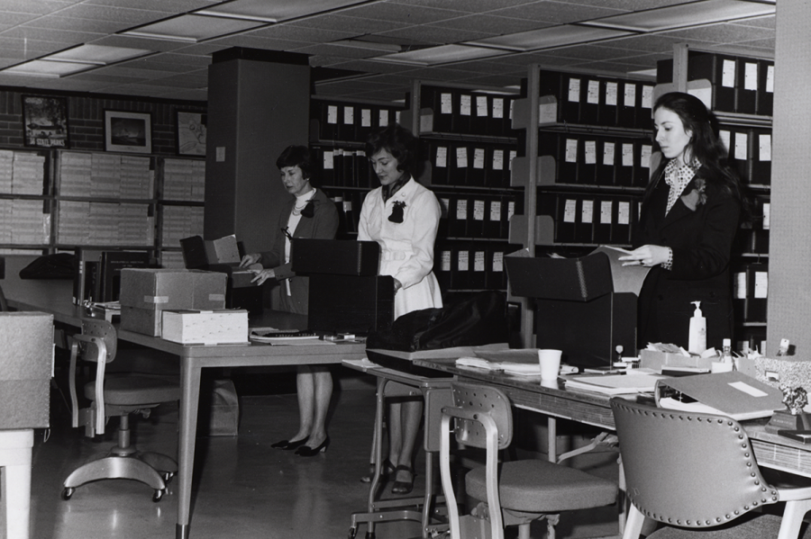 Black and white photo from 1970s of women looking through library archive boxes