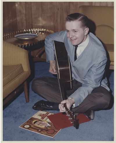 Young Bill Anderson sitting on the floor playing a guitar