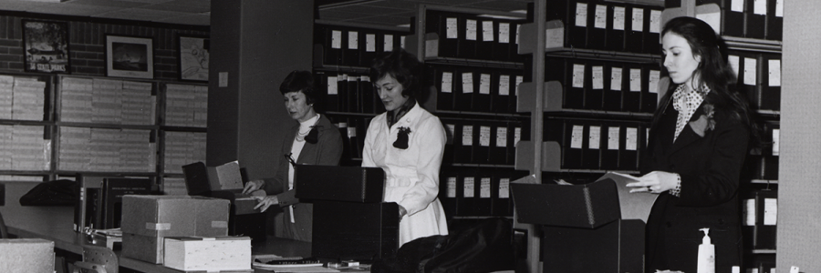 Three women looking a folders in the library