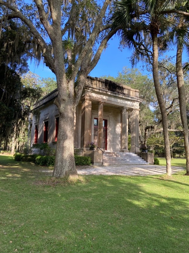 The DeRenne Library, a small but beautiful stone building with columns, shown in dappled shade from surrounding trees
