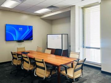 A study room with a large table and chairs plus a large LCD screen mounted on the wall.